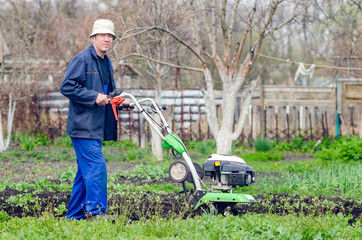 A man plows the land with a cultivator in a spring garden