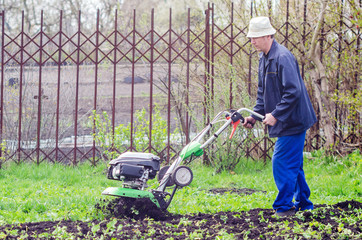 A man plows the land with a cultivator in a spring garden