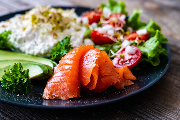 Breakfast - smoked salmon, cottage cheese, avocado and vegetable salad on wooden table
