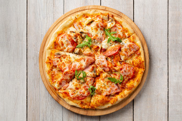 Tasty pizza with ham, mushrooms, tomatoes and arugula on wooden cutting board on white background.