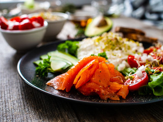 Breakfast - smoked salmon, cottage cheese, avocado and vegetable salad on wooden table
