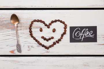 Smiley face with head in shape of heart and teaspoon. White wood background.