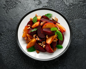 Vegan Plum, beet salad with pecan nuts, mint and herbs on rustic black table