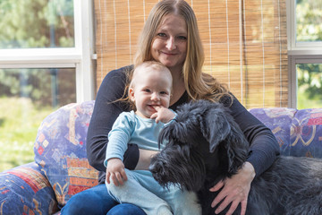 Young mother with her smiling baby boy and Big Black Schnauzer Dog together. 