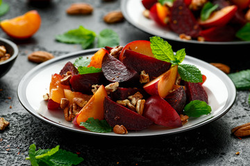 Vegan Plum, beet salad with pecan nuts, mint and herbs on rustic black table