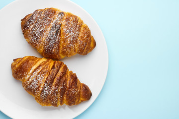 Freshly baked italian croissants on a white plate on the blue background with copy space. Concept of advertisement of traditional pastry.