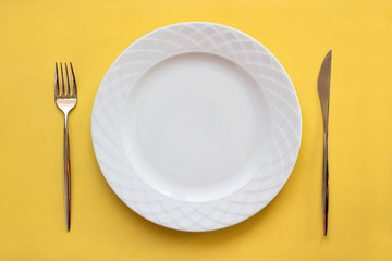 Empty plate, fork and knife over yellow background.