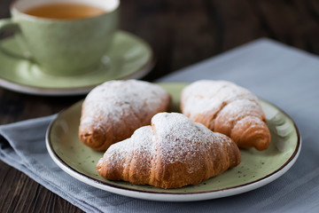 Cup of green tea and a croissant on brown wooden background. Soft focus.