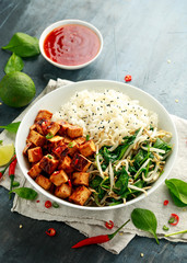 Fried tofu in sweet chilli glaze served with rice, steamed spinach and beansprouts in white bowl. Vegetable healthy food
