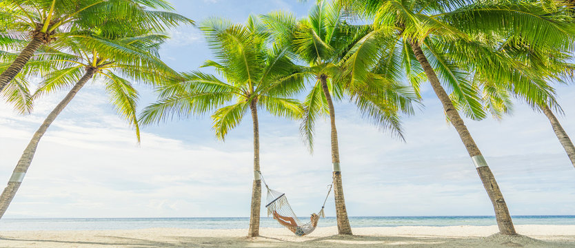 Woman lying on hammock between palms on the beautiful tropical beach. Travel and vacation concept. Banner and panoramic edition.