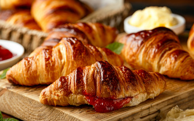 Freshly baked croissants with butter, strawberry jam and tea for breakfast or brunch