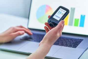 Diabetic patient using remote sensor and computer for control, examining and monitoring glucose blood levels graphs. Medical technology in diabetes treatment, healthcare