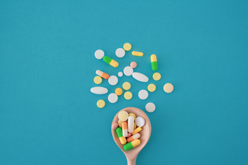 Colorful pills and capsules on a wooden spoon on a blue background,  pills are scattered in the center from bottom to top