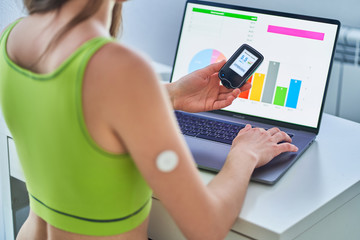 Diabetic patient using remote sensor and computer for online monitoring and examining glucose blood levels graphs. Diabetes control