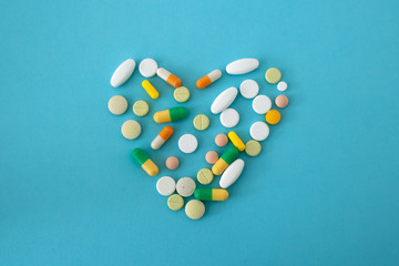colorful pills and capsules in the shape of a heart on a blue-green background located in the...
