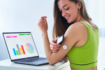Woman diabetics using remote sensor and computer for control, online monitoring and examining glucose blood levels graphs. Diabetes lifestyle - obrazy, fototapety, plakaty