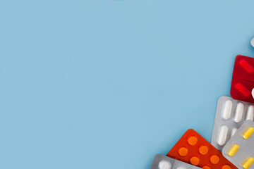 colorful tablets and capsules, tablets in the package, are evenly distributed on the right side on a blue background, with free space for text on the left and in the center