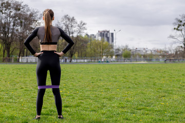 Obraz na płótnie Canvas Fitness girl workout with fitness elastic bands in black tracksuit outdoors