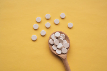 Fototapeta na wymiar round white tablets on a wooden spoon on a yellow background, tablets are scattered in the center from bottom to top