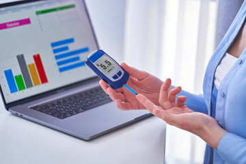 Diabetic patient checks blood glucose level using glucometer. Diabetes control and studying glucose graphs on a computer online at home