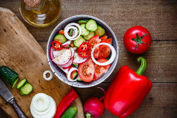 Salad of tomatoes cucumbers onions radishes avocado peppers on a wooden background.