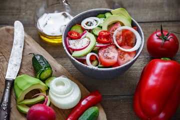 Salad of tomatoes cucumbers onions radishes avocado peppers on a wooden background.
