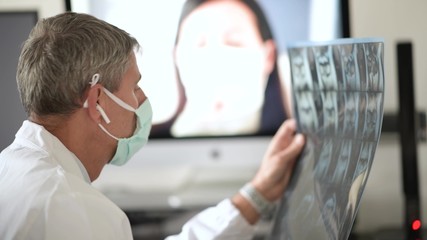 Video call in coronavirus times. Doctor wearing mask and examining xray scan visiting woman at home