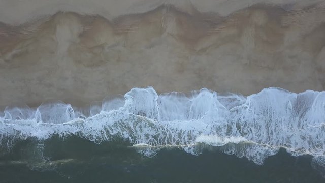 Flying over a sandy beach. Waves break on a sandy beach on the Atlantic coast, aerial View. Nazare, Portugal. (raw video).