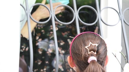 Coronavirus Quarantine. Depressed Woman In Protective Mask Waving to her Daughter Through Glass Door During Self-Isolation At Home