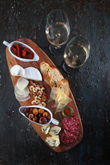 Snacks for wine. Cheese and cold cuts with nuts on a wooden Board. Textured aged dark background. The view from the top. Copy of the space.