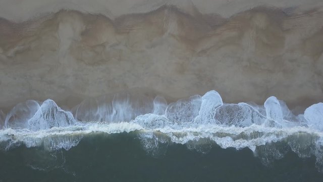Flying over a sandy beach. Waves break on a sandy beach on the Atlantic coast, aerial View. Nazare, Portugal. (raw video).