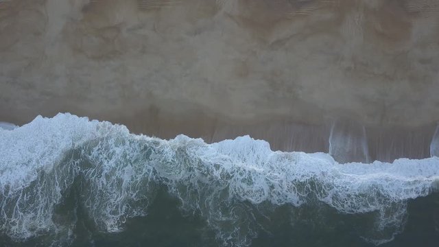 Flying over a sandy beach. Waves break on a sandy beach on the Atlantic coast, aerial View. Nazare, Portugal. (raw video).