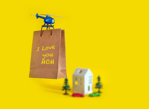 Yellow paper bag gift toy house tree delivery helicopter fly copy space background I love you mom