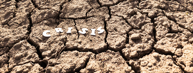 The word CRISIS in paper letters on the background of dry earth with cracks. Crisis concept. Banner.