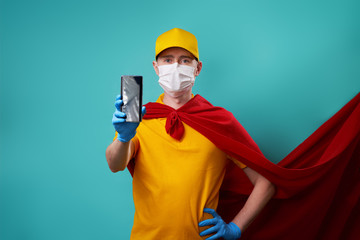 Fototapeta na wymiar Courier dressed in superhero cloak and medical mask holds smartphone in his hand.