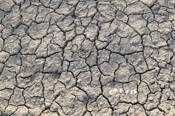 The word CRISIS in paper letters on the background of dry earth with cracks. Crisis concept.
