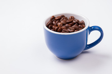 Blue cup full of coffee beans isolated on white. Close up mug filled with brown coffee seeds.