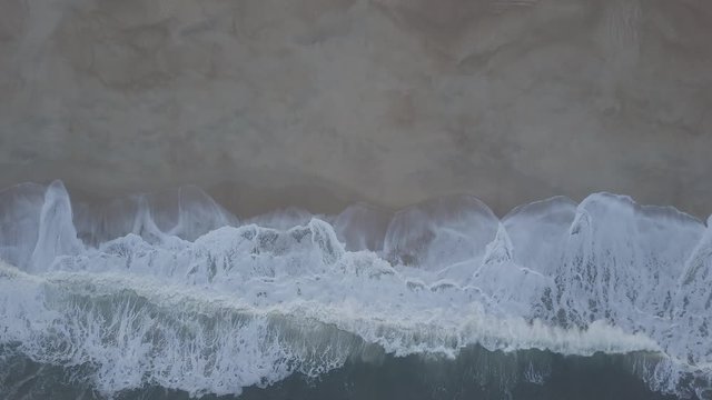 Flying over a sandy beach. Waves break on a sandy beach on the Atlantic coast, aerial View. Nazare, Portugal. (raw video).