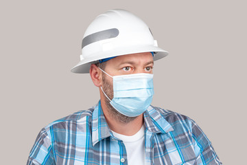 Engineer or construction worker with casual clothing and safety hard hat wears surgical face mask. Concept of new safety measures taken by companies to slow the spread of coronavirus among their staff