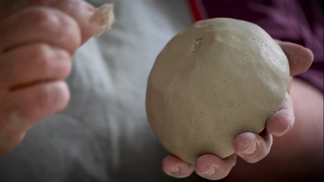 Hand dr&uuml;ckt einen Stempel mit Initialen in den Boden einer Schale aus weichem Ton