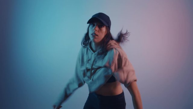 Trandy woman in cap dancing in Multi-Colours Neon Lighting room at night. Portrait of Young Stylish Woman Dancing at Party in nightclub