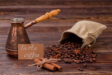 Coffee beans in a sack with pot and cinnamon tubes on wood. Still life tasty coffee concept.