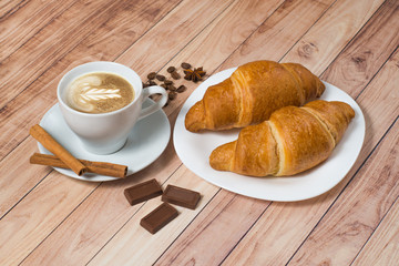 Closeup breakfast with cup of coffee, croissants, beans, chocolate and cinnamon. Coffee cup latte art. Space for text