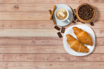 Top view with cup of coffee, croissants, beans, chocolate and cinnamon. Coffee cup latte art. Flat lay breakfast on wooden background. Space for text