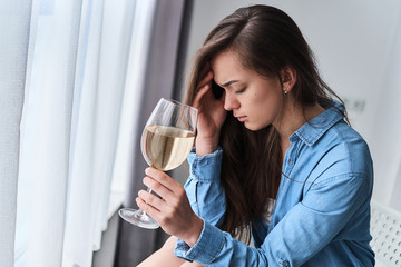Young upset sad depressed stressed drinking woman with wine glass suffers from a hangover and headache. Female alcoholism and life problems, alcohol addiction during depression and worries