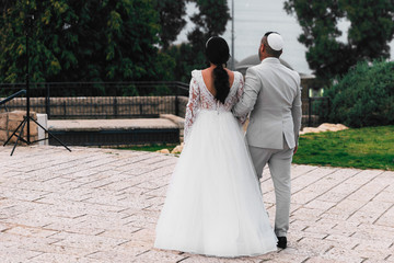 The bride and groom in a bale on back in Israel. Jewish wedding. Newlyweds are photographed during a wedding. Man and woman holding hands, rear view. Tripod with flash in front of the newlyweds