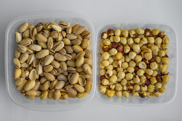 Top closeup view of delicious crispy snacks such as salted dry pistachio nuts and fried hazelnuts which are stored in plastic transparent containers