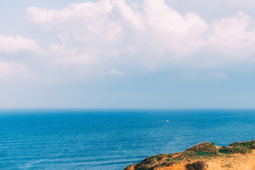 Great landscape view on Mediterranean Sea with a piece of land and a small yacht sailing in the distance. Fuzzy skyline and white beautiful clouds. Postcard, desktop wallpaper. Blue water