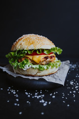 Appetizing fresh homemade burger, with chicken cutlet, lettuce, tomatoes, cheese and sauce. On a wooden board on a black background