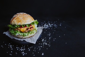 Appetizing fresh homemade burger, with chicken cutlet, lettuce, tomatoes, cheese and sauce. On a wooden board on a black background